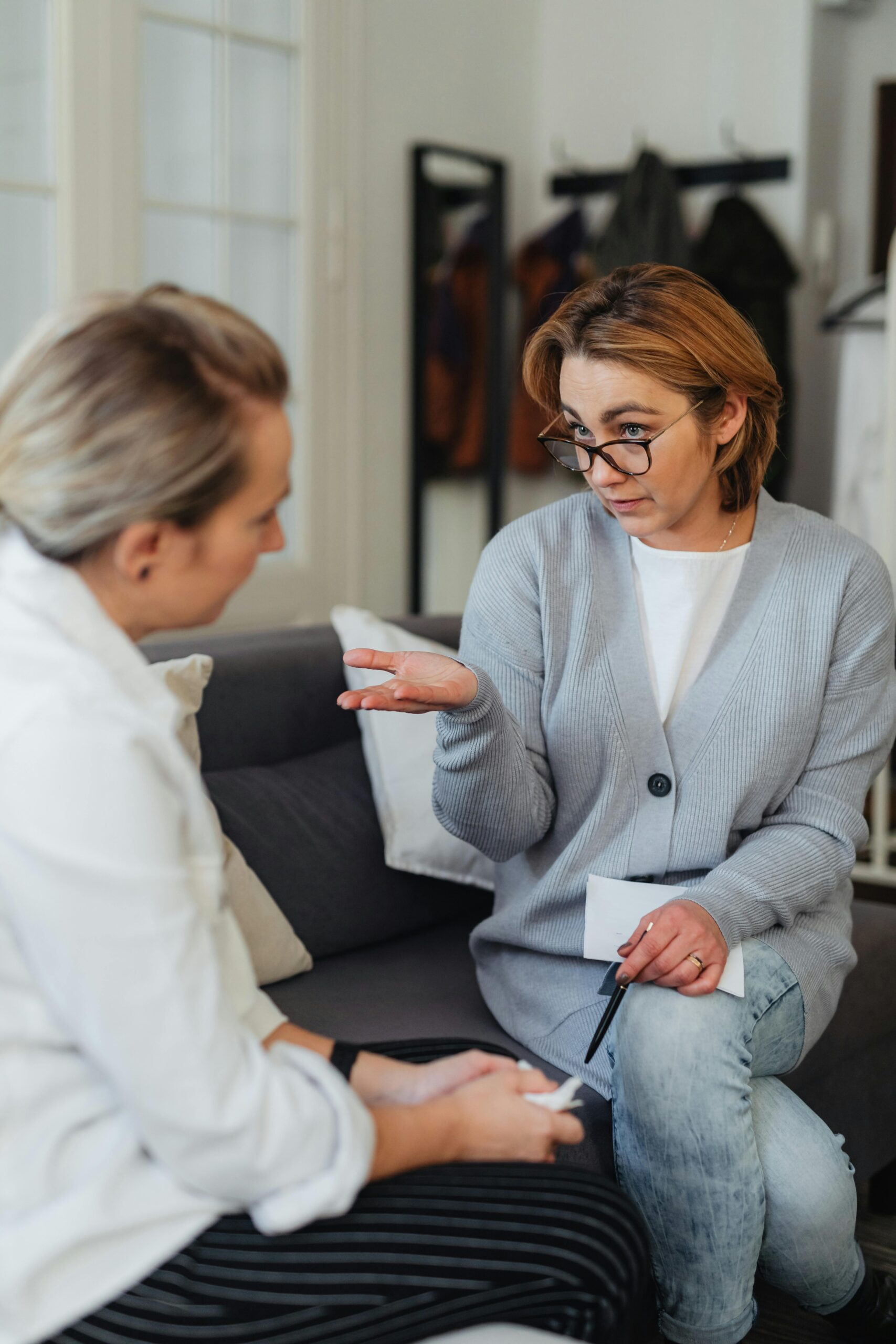 Two women engaged in a serious conversation on a couch, discussing important matters.