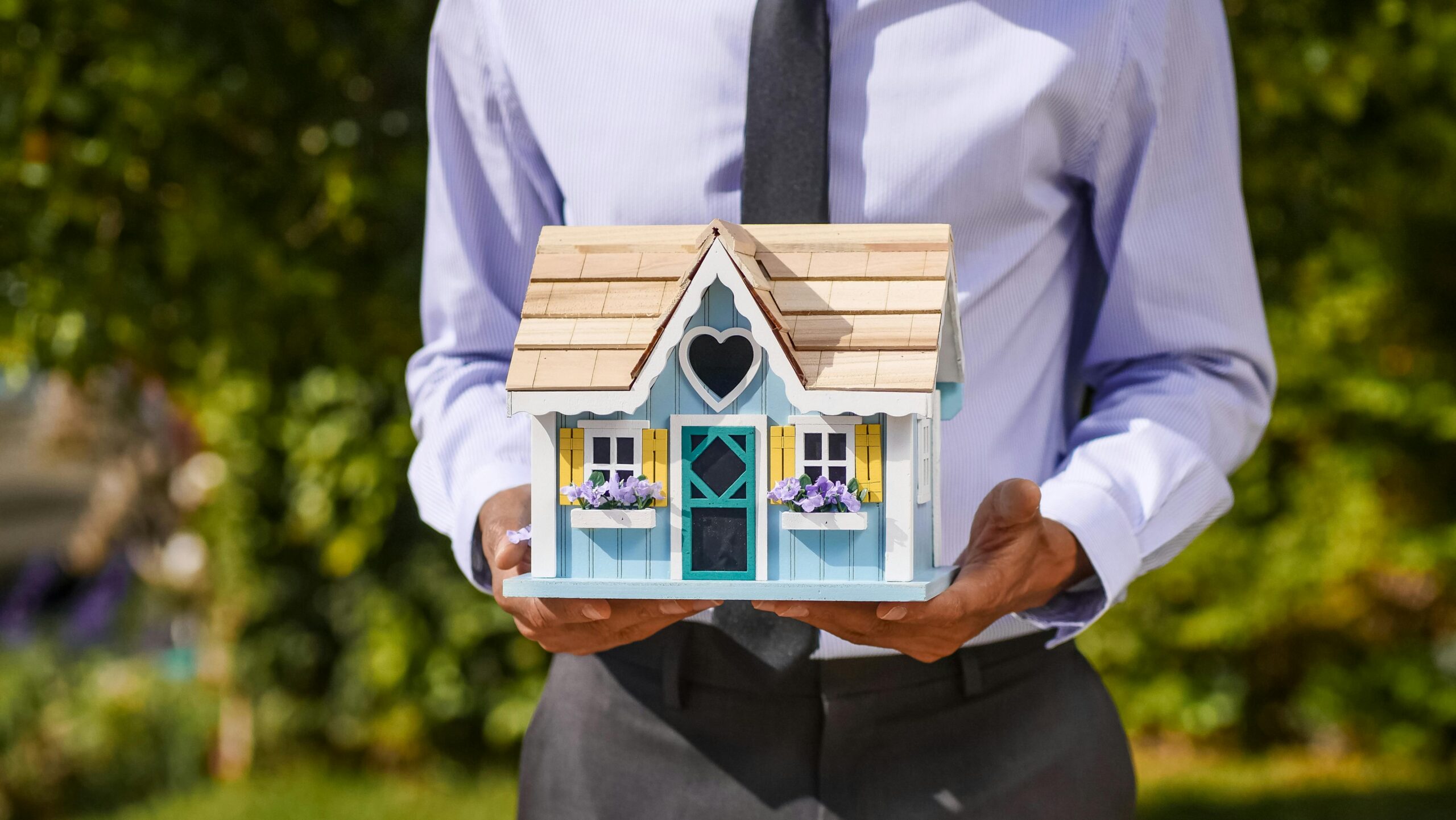Businessman holding a model house symbolizing real estate investment.