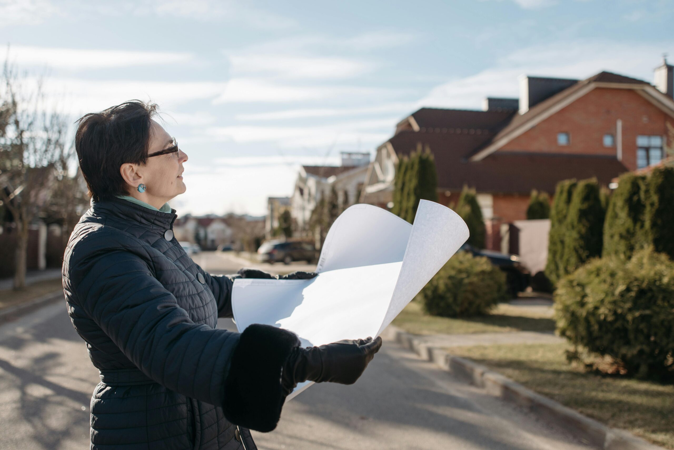 Woman in a blue jacket reviewing architectural plans outdoors on a sunny day.