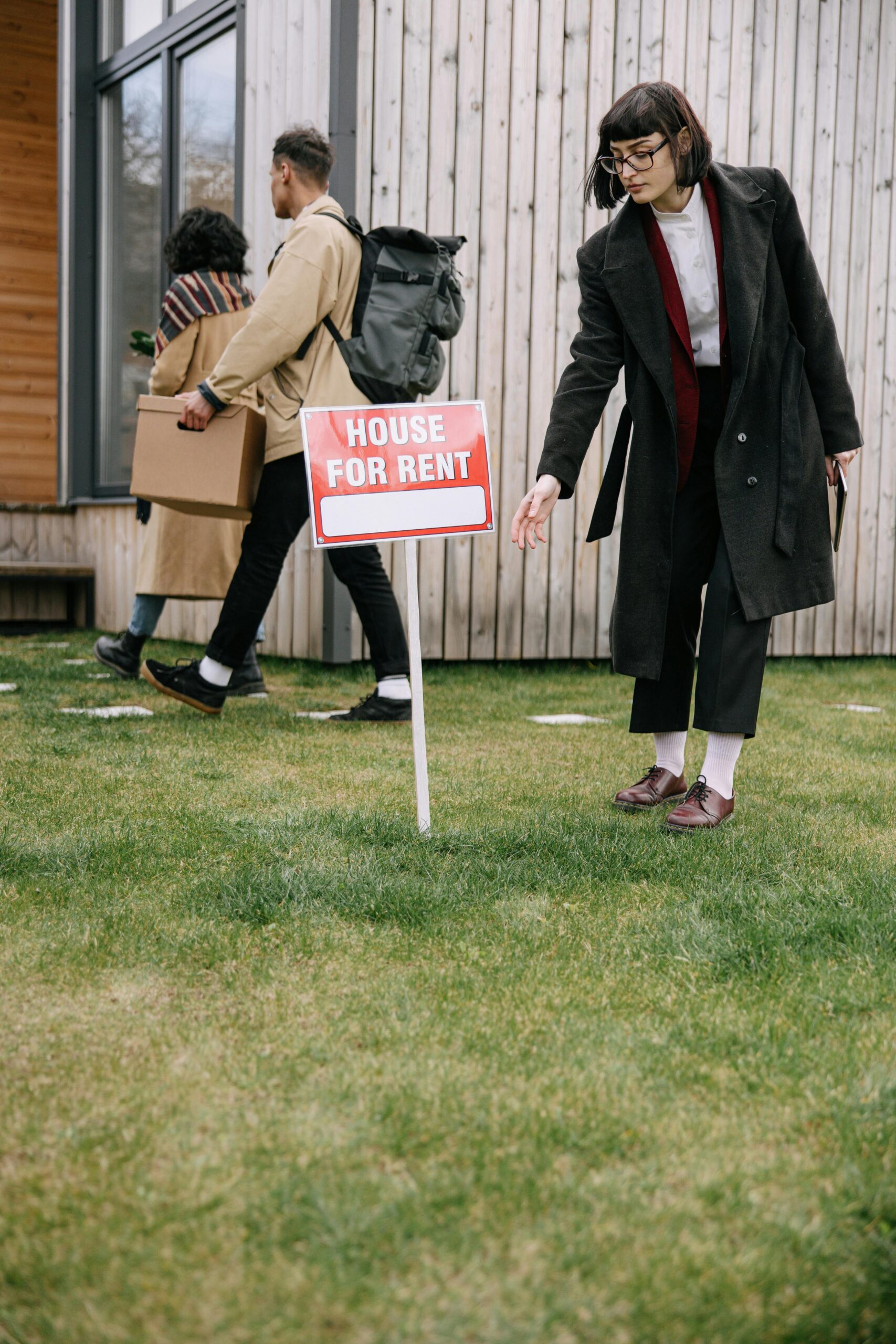 A group of adults inspecting a house for rent sign outside an apartment building while moving in.